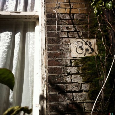 black old fashion house number 83 on a brick wall surrounded by dry branches in Amsterdam