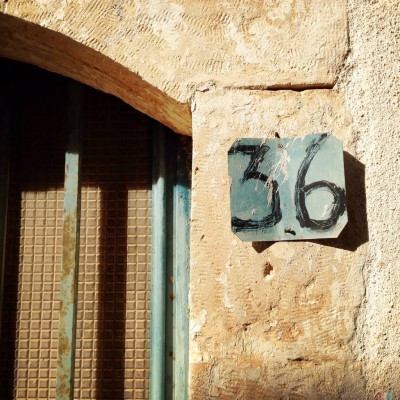 black hand written on green metal plate house number 36, on a stone wall on Crete