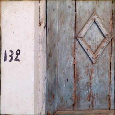 black handwritten house number 132 next to a blue old window on Crete