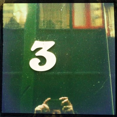 white number 3 on a green shiny door reflecting the surroundings. In Amsterdam