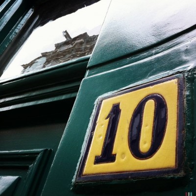 yellow house number 10 on a dark green door next to a city reflections in Amsterdam