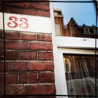red house number 33 on a brick wall next to a window reflection in Amsterdam
