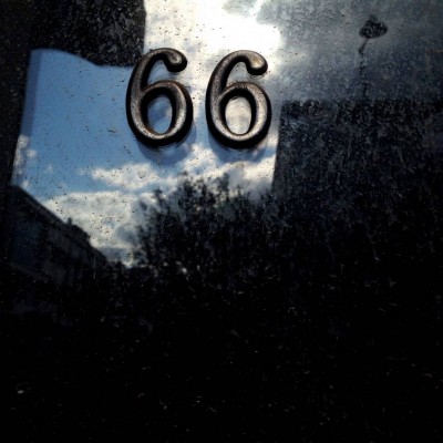 metallic house number 66 on a dusty window with the reflections of the city, on Crete