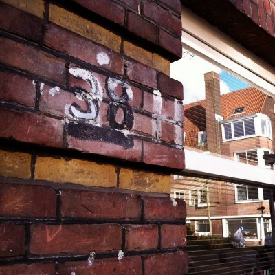 handwritten house number 38 on a brick wall next to a window reflection in Amsterdam