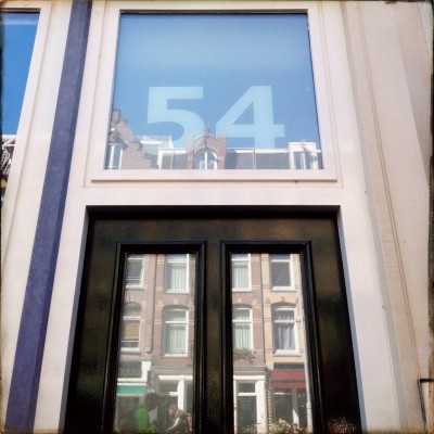 house number 54 on a glass door facade reflecting Amsterdam