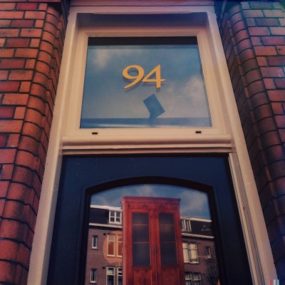 house number 94 on the glass of the door facade that reflects the buildings of the other side, in Amsterdam