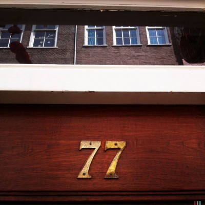 golden color metallic house number 77 on a wooden door facade, in Amsterdam