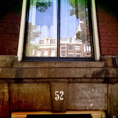 white number 52 under a house window that reflects the city of Amsterdam