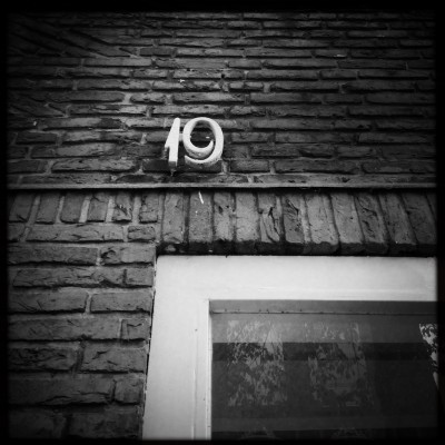 b&w photo of a metal house number 19 on a brick wall in Amstrdam