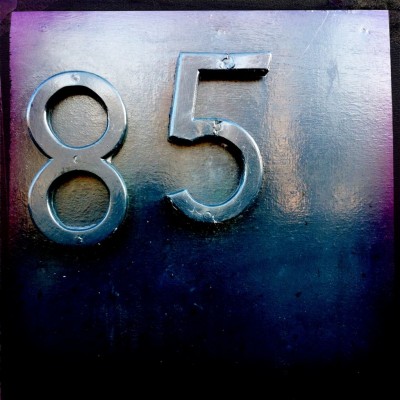 Dark grey house number 85 on a door in Amsterdam